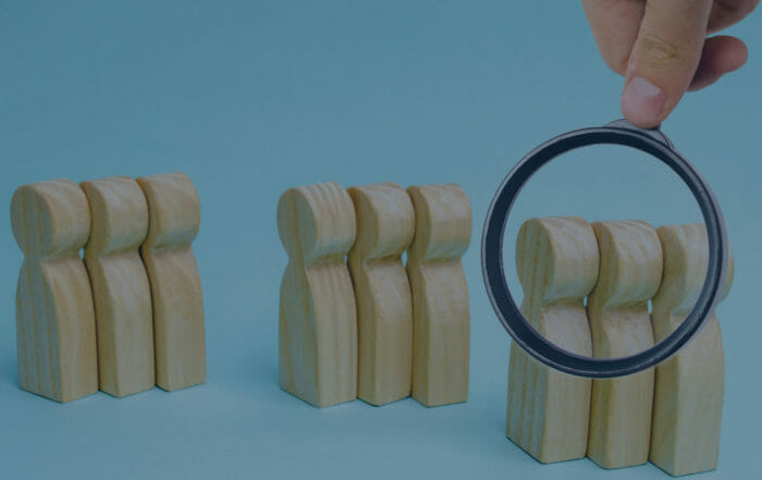 Image of wooden clothespins in three groups of three and a magnifying glass is being held over the group on the right side of the image to convey getting to know your consumer